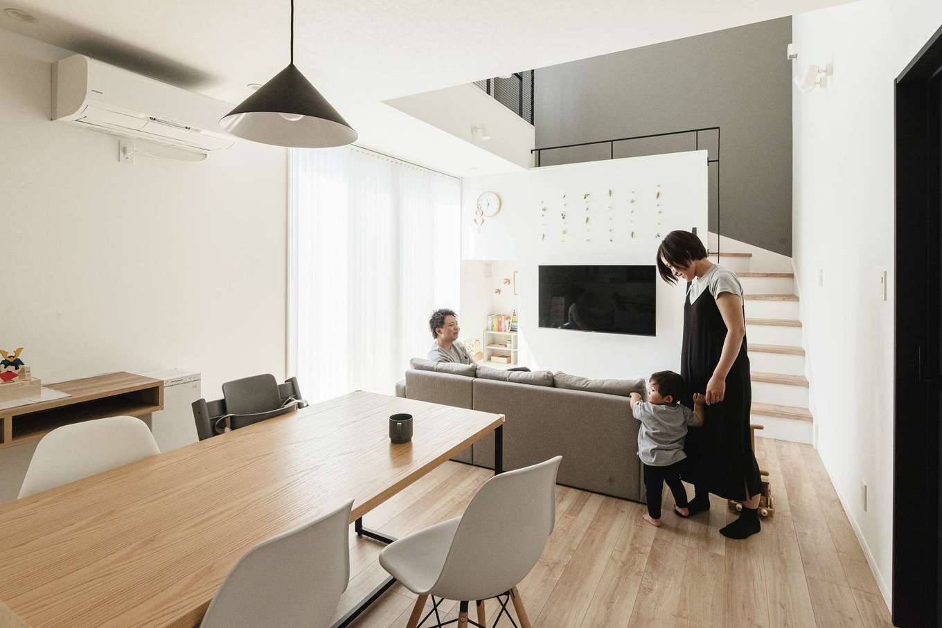 HAPPY HOUSE（山田工務店）【1000万円台、デザイン住宅、子育て】大らかさ、ナチュラル感、そしてA夫妻のセンスが溶け合うLDK。大きな窓と吹き抜けから運ばれるたっぷりの光が家族のひとときをやさしく包む。グレーの壁と太さや間隔にまでこだわった階段のアイアンが開放的な空間にほどよい落ち着きを添えている