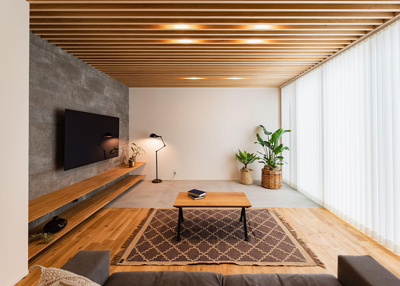 住家 JYUKA【デザイン住宅、間取り、平屋】外観の閉じた印象から一転、リビングは大きな窓を通じて明るさで満たされる。土間は、お気に入りのアウトドアグッズや、水のしみ出しが気になる観葉植物を置くのにもピッタリ。そのままタイルデッキへとつながり、季節ごとの豊かさや楽しさがもたらされる