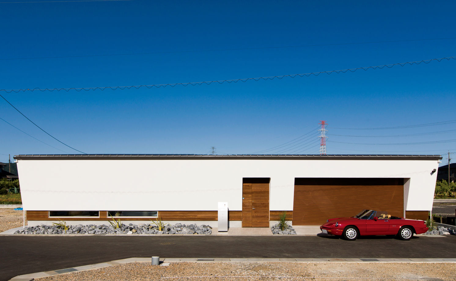 チェックハウス｜モダンなデザインの平屋建築の外観。白と木調のコントラストが美しく、駐車スペースには赤い車が並ぶシンプルでスタイリッシュなデザイン。