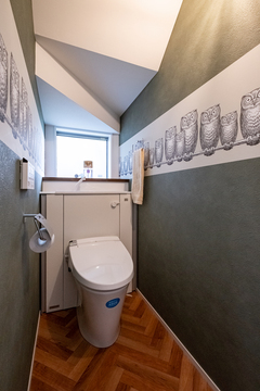 ふくろう柄の輸入クロスがかわいいトイレは階段下スペースを活用。タンク部分を収納に隠し、スッキリさせた