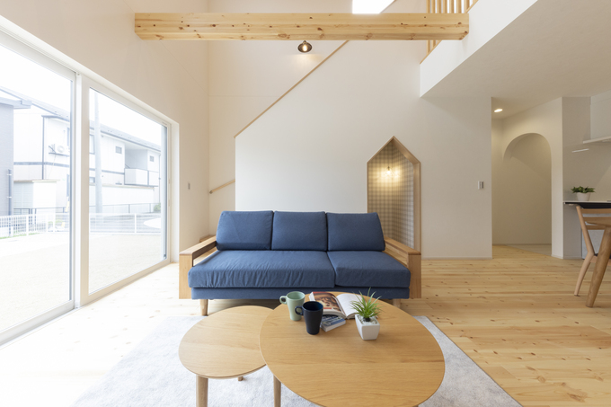 吹き抜けが開放感を与えるリビングスペース。大型の窓から自然光が差し込み、木材の暖かみが感じられるシンプルでモダンなデザイン。