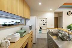 ステンレス製システムキッチンの後ろは、リビングと同じタモ材を使った収納棚を造作。フタが開く高さを計算し、ごみ箱をぴったり収納。マグネット式のニッチ＆マガジンラックで散らかりがちなリモコンや雑誌もすっきり