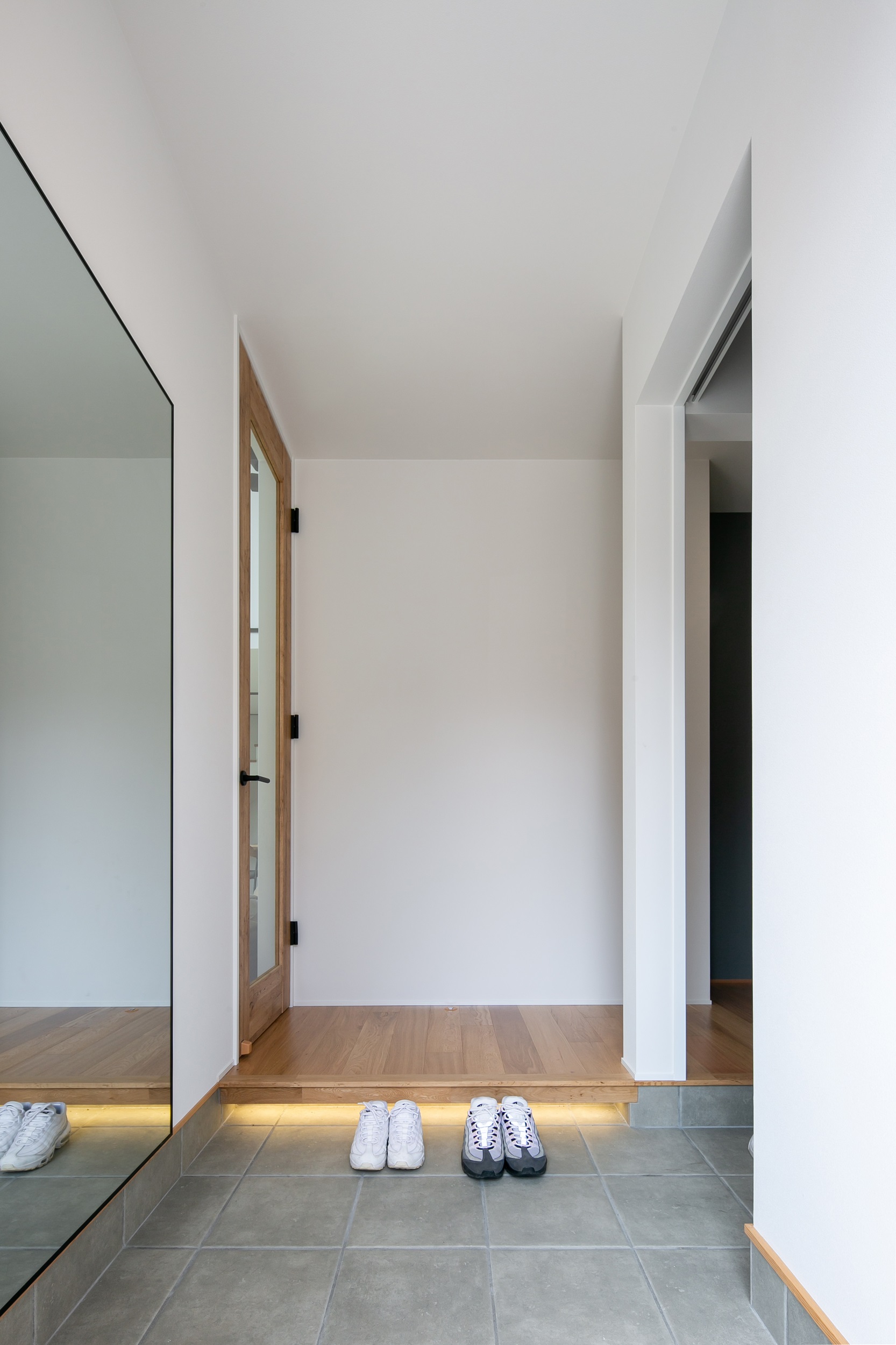 シンプル｜1.5帖の玄関スペース。
玄関に姿見を付けたいとのご要望で大きな鏡を施工。
框下には足元を照らす間接照明で、スタイリッシュな印象に仕上がった。