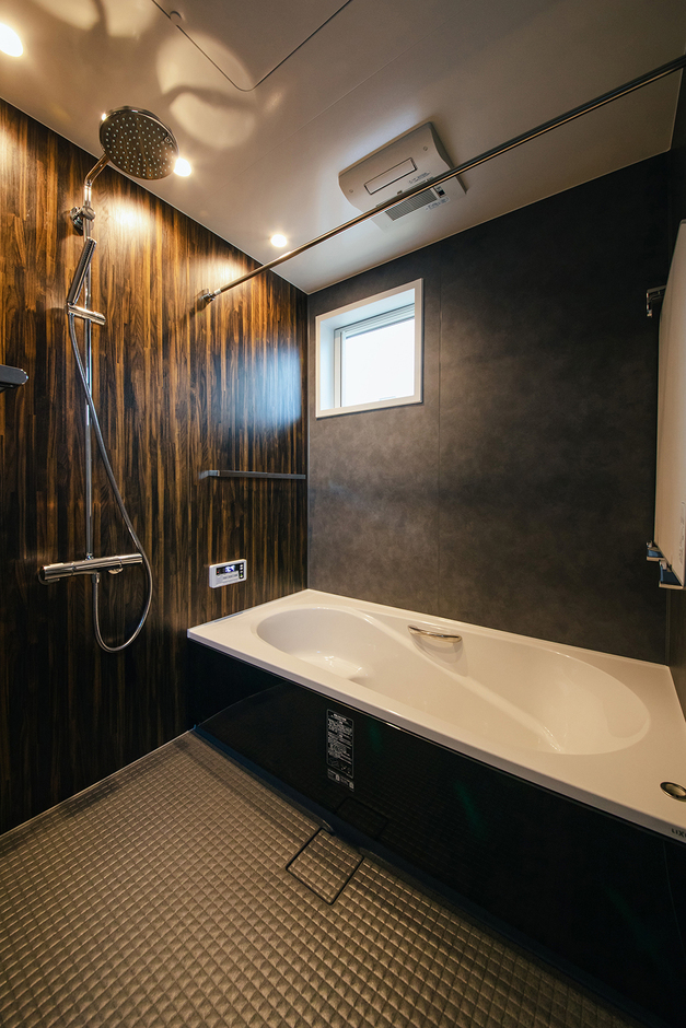 木目調と黒のコントラストが美しいバスルーム。広々とした浴槽とシャワーヘッドが備わり、リラックスしたバスタイムを楽しめる