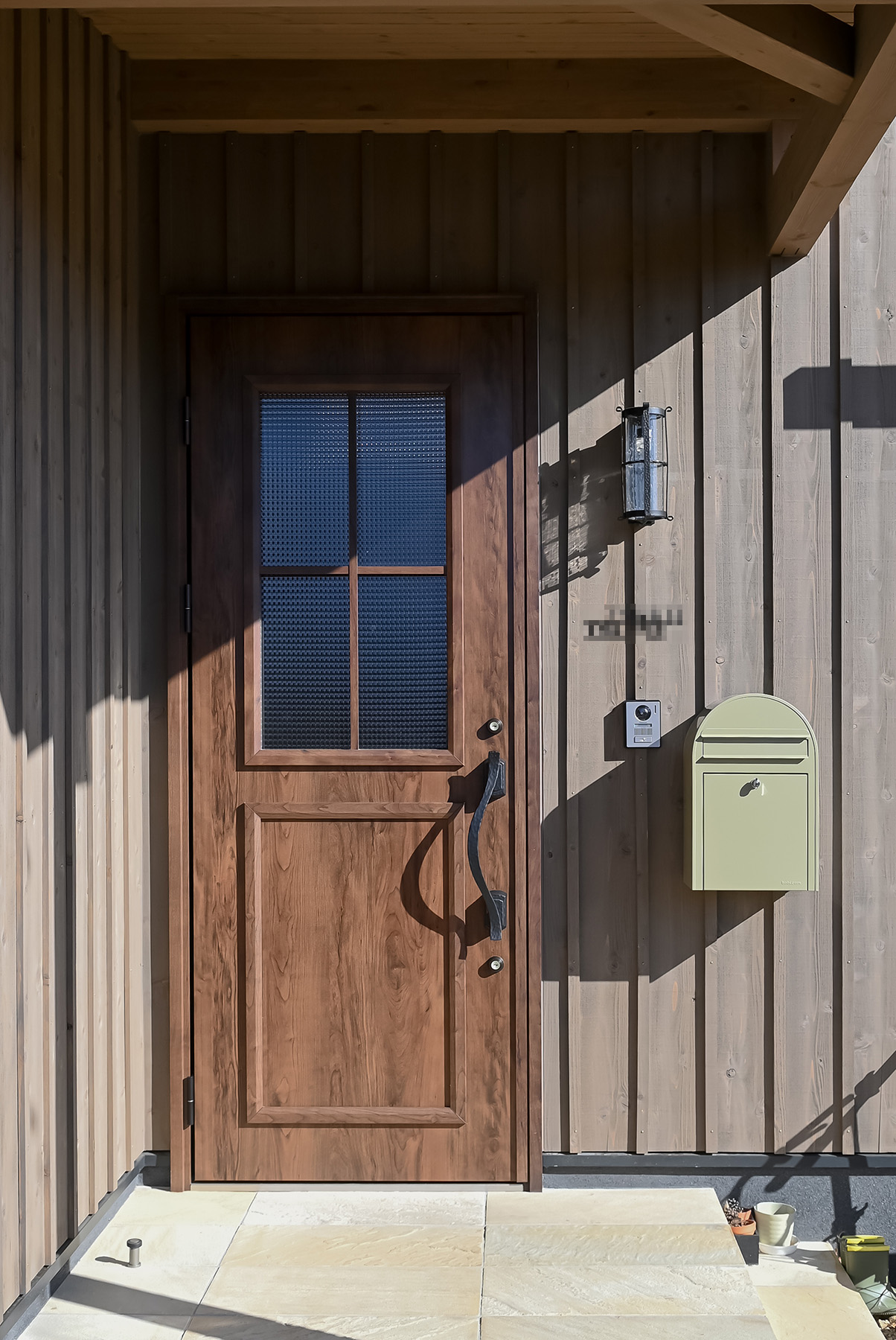 ネクストハウスデザイン｜自然素材の木を使ったシンプルで落ち着いたデザインの玄関。玄関灯とポストがアクセントになり、訪れる人を暖かく迎えるエントランス。