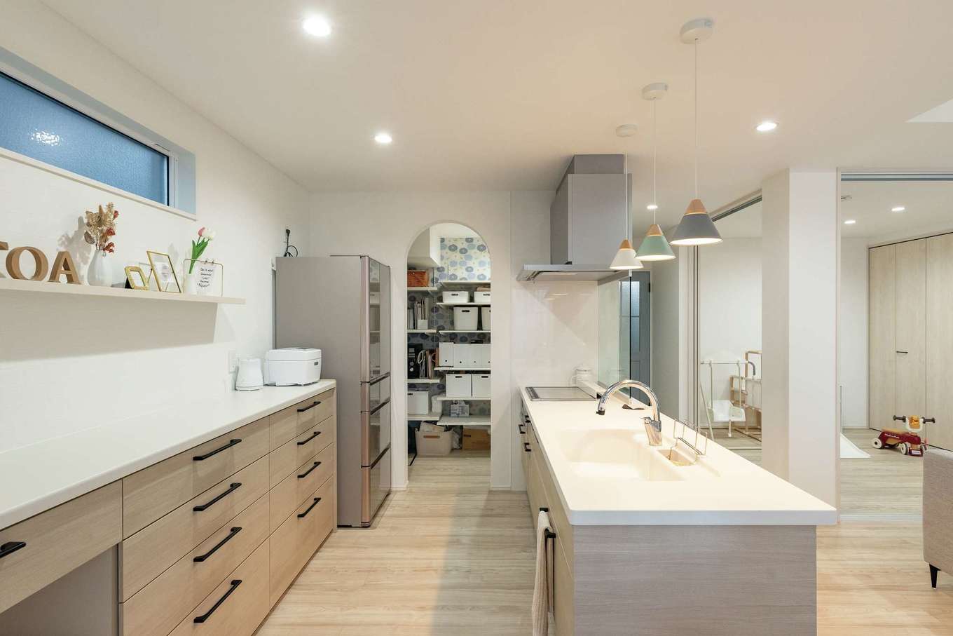 HAPPY HOUSE（山田工務店）【デザイン住宅、子育て、間取り】あえて吊り戸棚をやめて、スッキリとしたキッチンが完成。造作の棚は、現場で細かく打合せをして幅や高さを決定した。パントリーは可動棚による収納力はもちろん、入口のRやクロスなど希望通りの仕上がり。キッチンに立てばLDK全体が見渡せ、家族が階段を上り下りする気配も届く。右手の和室は間仕切りも可能で、幅広い用途を受け止める