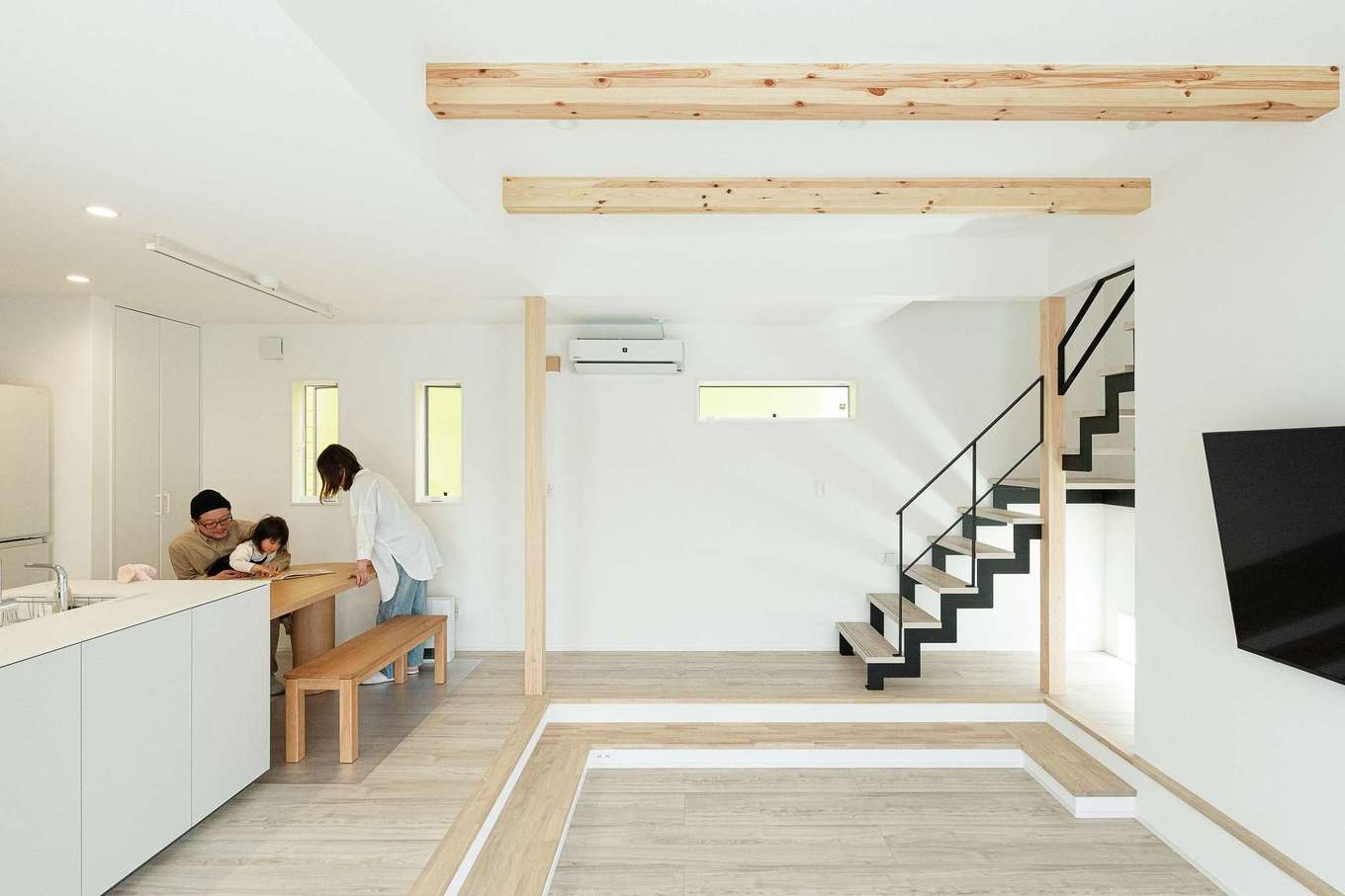 三和建設【デザイン住宅、子育て、間取り】リビングをぐるりと取り囲むように段差を付けたアンダーリビング。空間にメリハリが付き、人が集まる時には腰掛けて顔が向き合うので会話も弾む。階段のアイアンは黒にすることで引き締め効果を発揮。階段下には地窓をつけ、将来犬を飼うための専用スペースを用意した