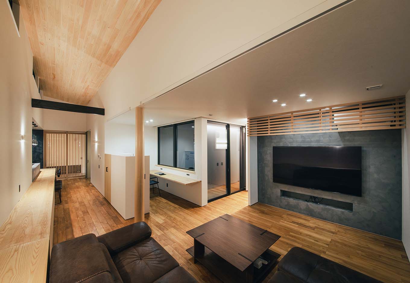 平屋建築ブルーハウス【デザイン住宅、建築家、平屋】ダイニングキッチンとリビングを壁で完全に仕切らずにオープンにすることで、空間のつながりと開放感を確保している。リビングのアクセントウォールはヘイムスペイントでグレーに仕上げ、キッチンと関連性を持たせている。書斎コーナーの手前には、耐震性を考慮して丸太柱を設けた