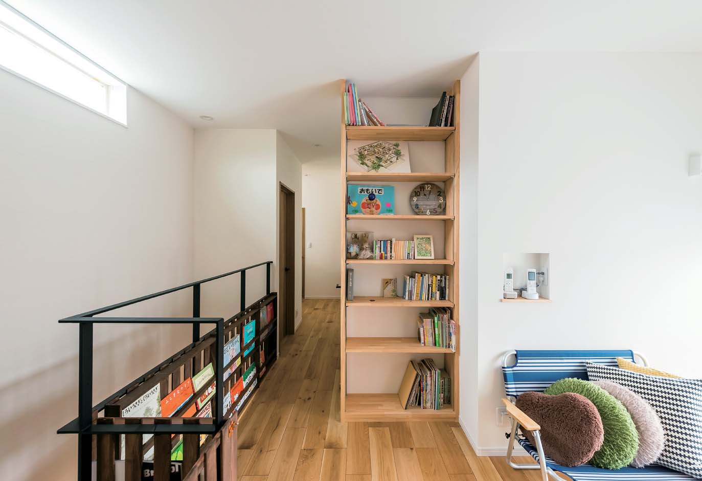 アトリエサクラ【子育て、間取り、ガレージ】2階のホールは、本棚を造作したライブラリーで家族のくつろぎの空間に。アイアンの手すり部分を活用したご主人お手製のマガジンラックもナイスアイデア