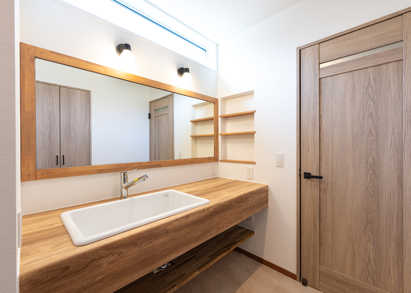 丸宗建設【デザイン住宅、収納力、間取り】脱衣室と洗面脱衣室を分けて配置。ワイドな鏡と洗面台は造作。ハイサイドライトからの光が安定的に差し込み、明るい空間に