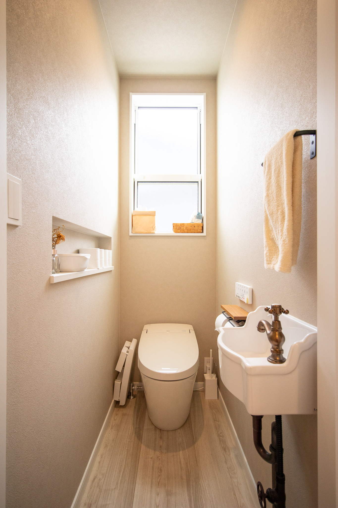 コンチネンタルホーム｜コンパクトながら明るく清潔感のあるトイレ空間。窓からの自然光が心地よく、シンプルなデザインとオープン棚が使いやすい。