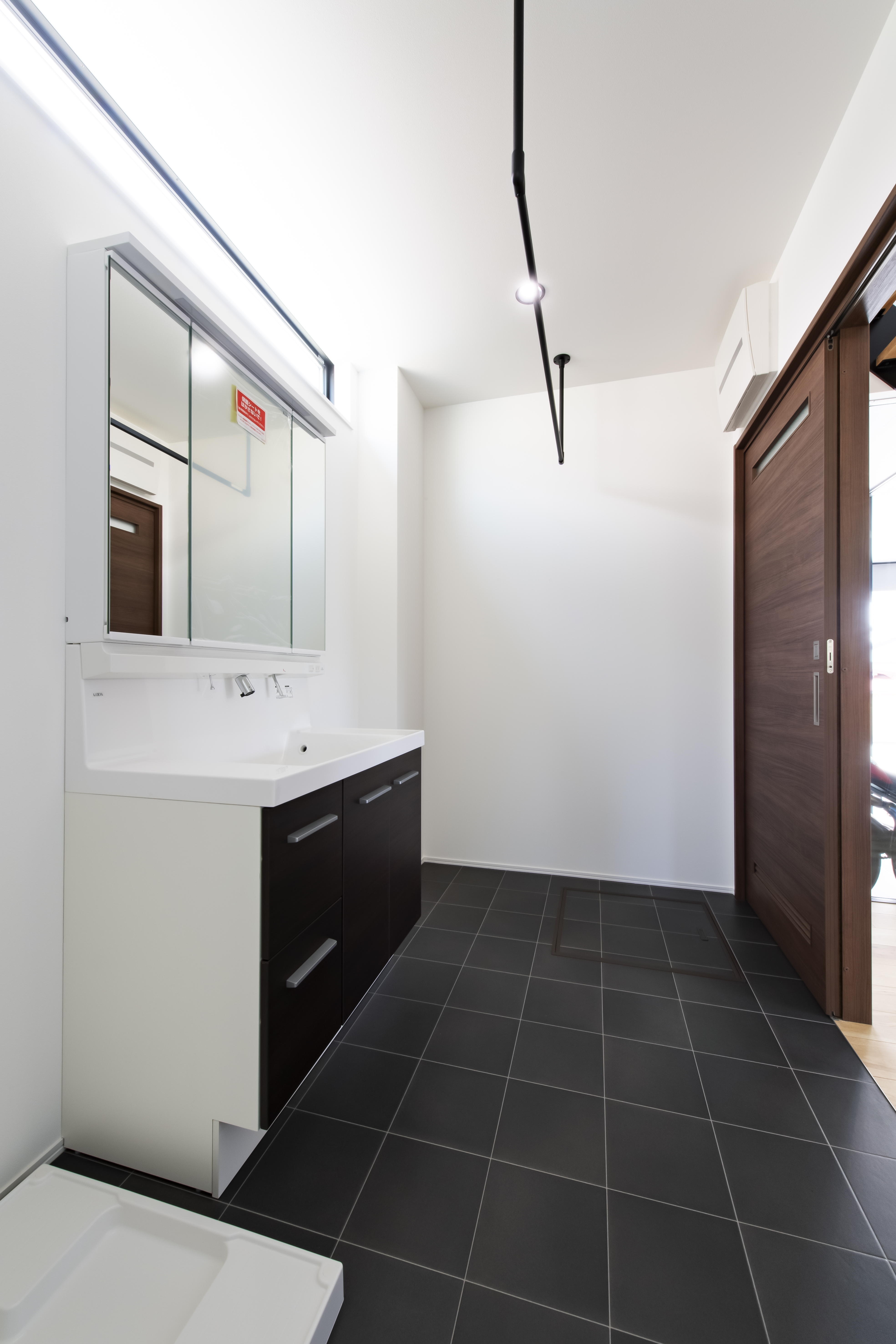 スズイチ｜シンプルで洗練された設計の洗面スペース。ダークタイルの床が落ち着きを感じさせ、清潔な印象が漂う。