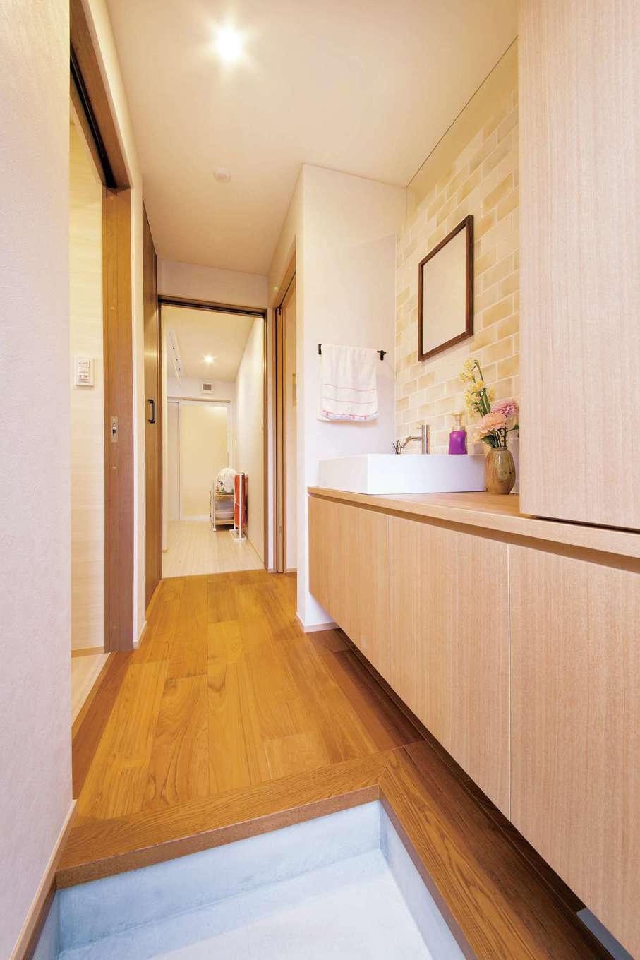 神谷綜合建設 カミヤの家【子育て、自然素材、スキップフロア】ダイニングキッチンの裏側には、浴室やトイレをまとめてレイアウト。洗濯機のある脱衣室から写真手前にある物干し場へ続く動線が便利。外に出したトイレの手洗い場の上部を透明の板にすることで、LDKともゆるやかにつながる