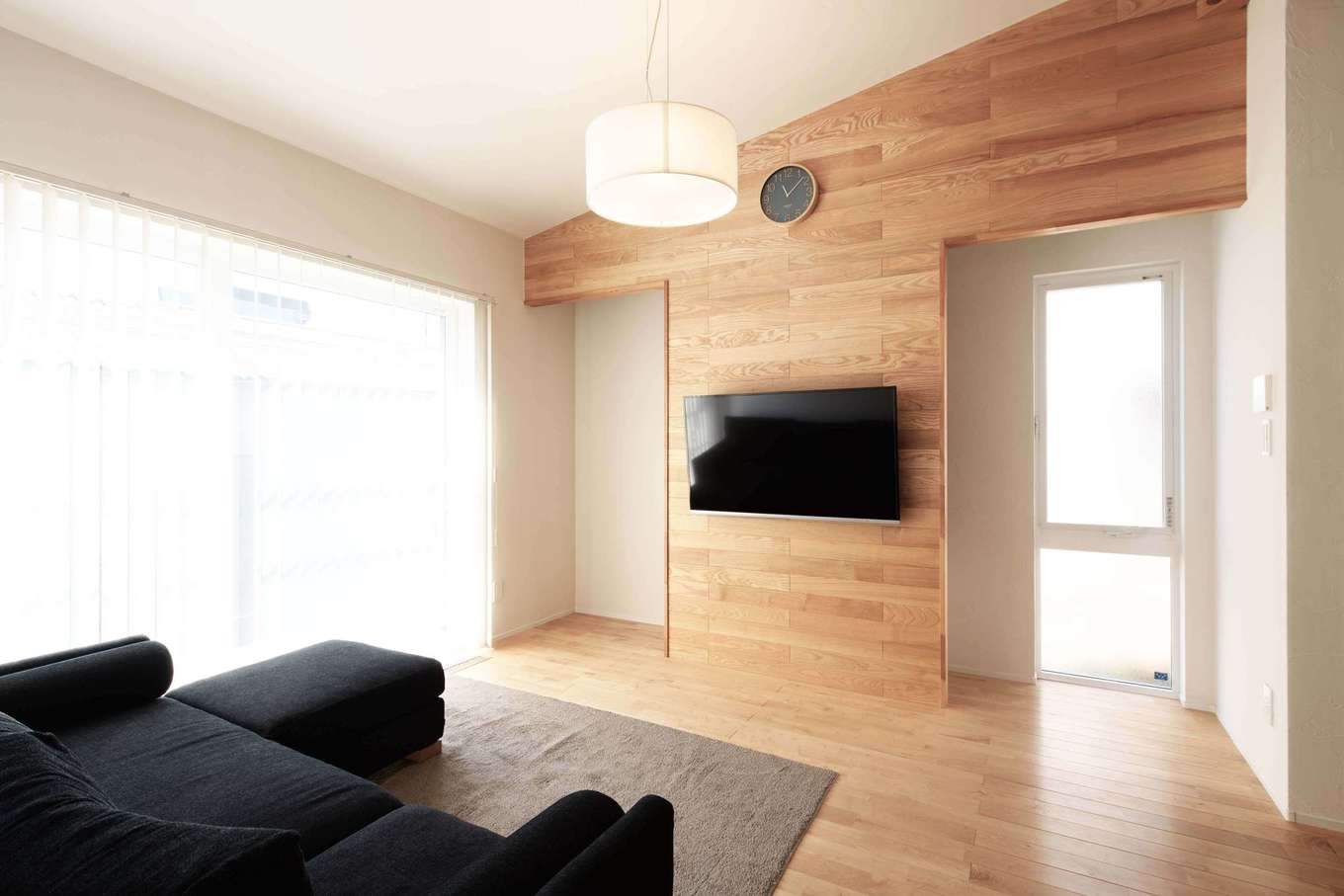 平屋建築ブルーハウス【デザイン住宅、子育て、平屋】自然素材に癒されながら、ゆったりくつろげるリビング。板張りのアクセントウォールと勾配天井の緩やかなカーブが、室内の意匠性を高めている。壁の背面に収納スペースを確保したことで雑多な生活用品が片付き、リビングをいつも美しく保つことができる