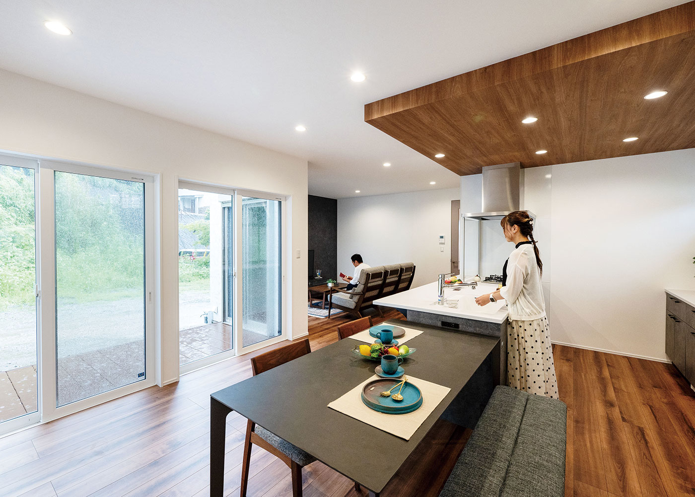 irohaco （アヴァンス）【高級住宅、夫婦で暮らす、平屋】庭の景色を眺めながら料理できるキッチン。木目調の下り天井がニュアンスを与える。ダイニングテーブルをキッチンと横並びにして、なおかつワークスペースを広く取ったことで家事効率もUP