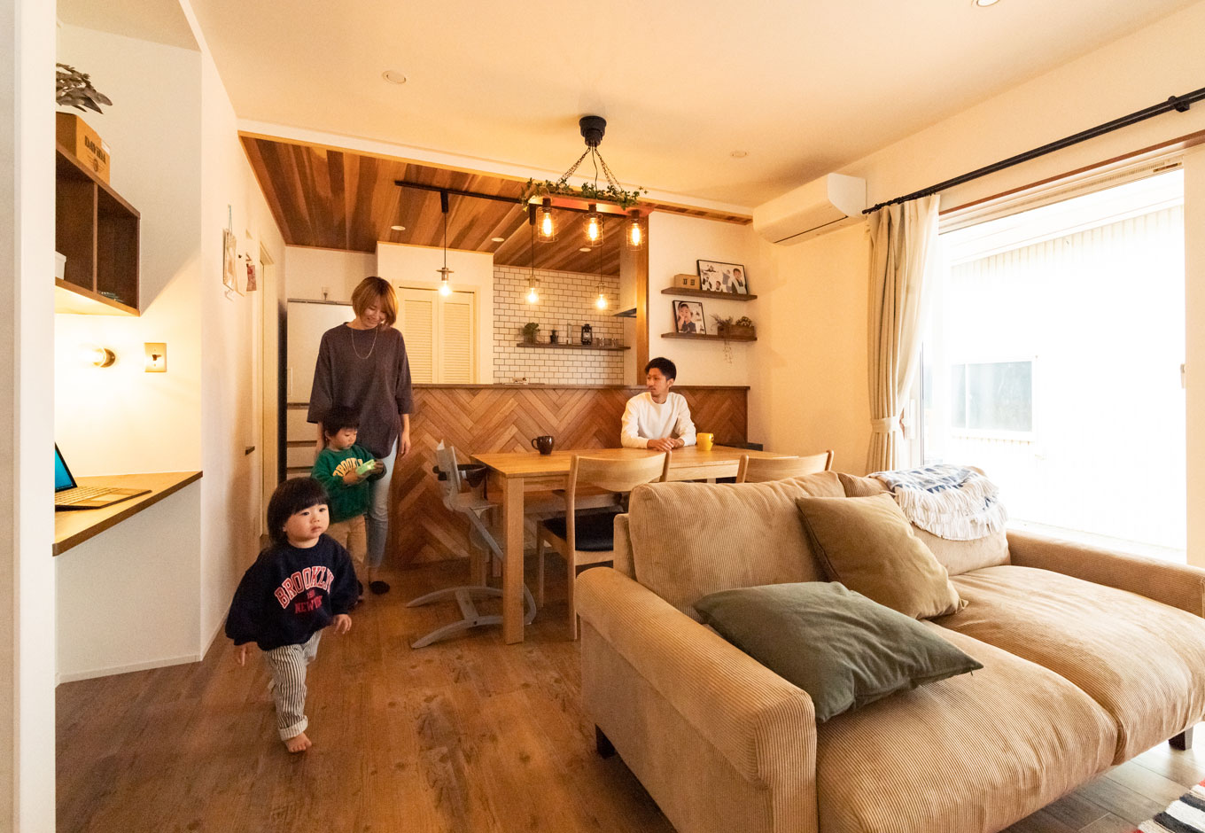 ホームプラザ大東【デザイン住宅、子育て、二世帯住宅】大きな窓を通してカバードポーチがつながり、LDKには実際の広さ以上の開放感がもたらされている。キッチンからはリビングやデッキはもちろん、玄関の出入りや階段の上り下りの気配まで届き、自然な会話が育まれていく。左手の造作カウンターは、パパのパソコンや将来の宿題に