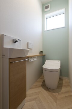 清潔感あふれるトイレ空間。明るい木目調の収納と緑のアクセントウォールが、落ち着きのある雰囲気を演出。