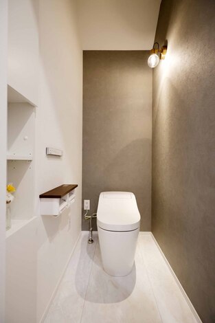 シンプルでモダンなデザインのトイレ空間。壁に設置された照明が温かみを加え、落ち着いた雰囲気を演出している。