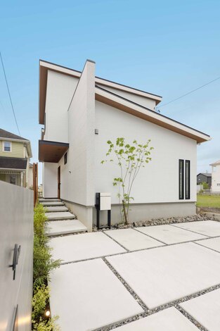 現代的なデザインの二階建て住宅の外観。シンプルで洗練されたあかるいカラー壁面が美しい。植栽がアクセントとなり、心地よい空間を演出している。