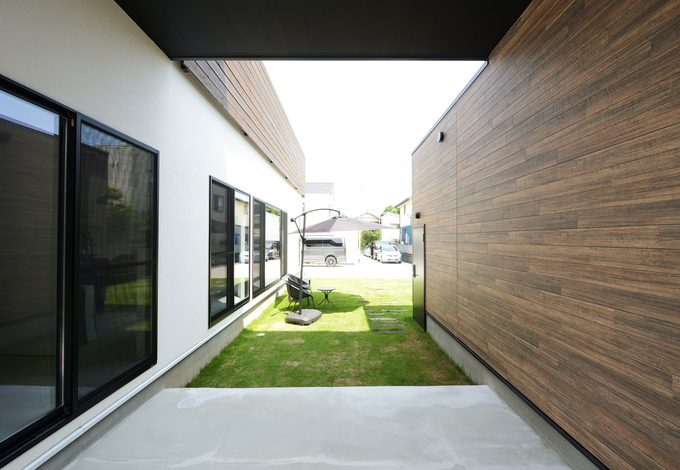 母屋と離れの事務所の間にある中庭空間。芝生の上に黒いパラソルとガーデンテーブルを置いて、リゾート気分で休日を楽しめる。コンクリートのテラス部分は屋根付きで、雨に濡れずに自宅から事務所へ移動できる