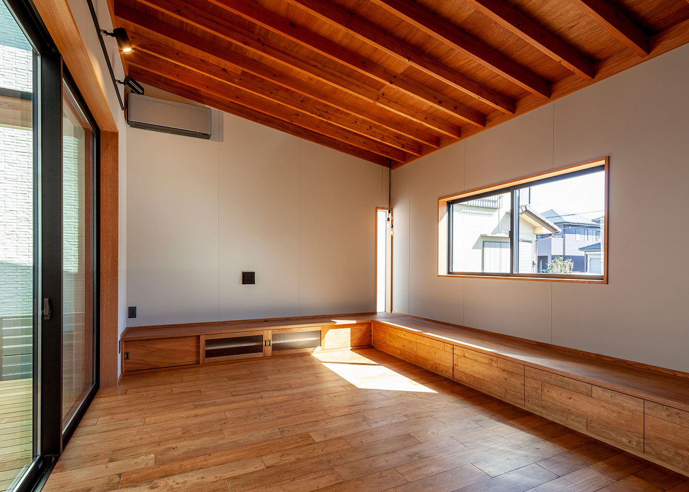 平成建設【デザイン住宅、子育て、間取り】リビング部分は家全体の日当たりを考えて、平屋建てで計画。この平屋建てを活かした勾配天井は、木を仕上げ材として使用することで、落ち着いた空間に。TVボードと4ｍを超えるベンチカウンターは大工の手技によるもので、使いやすいようサイズや機能性にもこだわっている