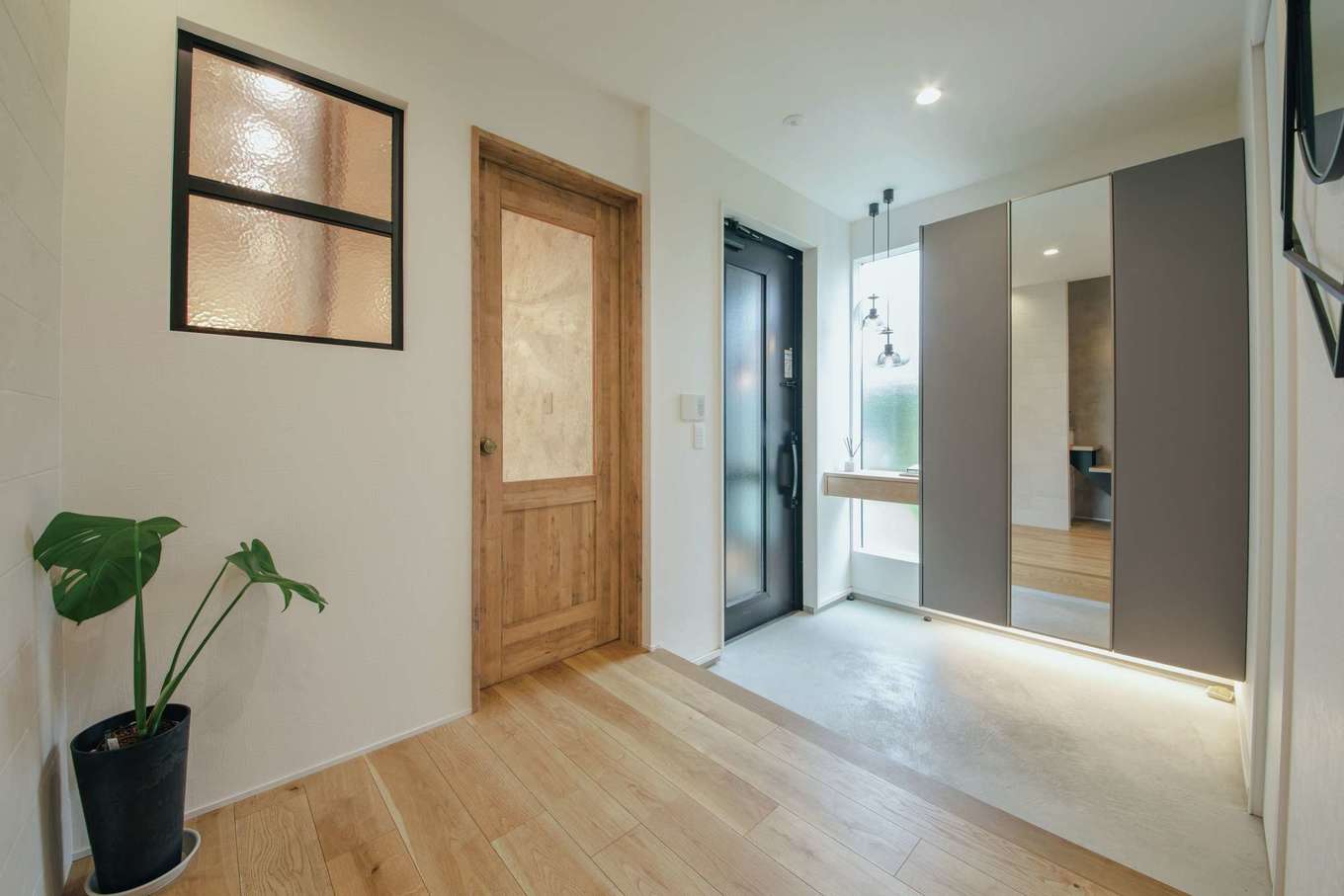 will建築工房【デザイン住宅、間取り、インテリア】自宅とヘアメイクスタジオ兼用の玄関。間接照明と姿見付きの収納を設け、開口部から明るさを招いている。木製ドアの先がヘアメイクスタジオのスペース