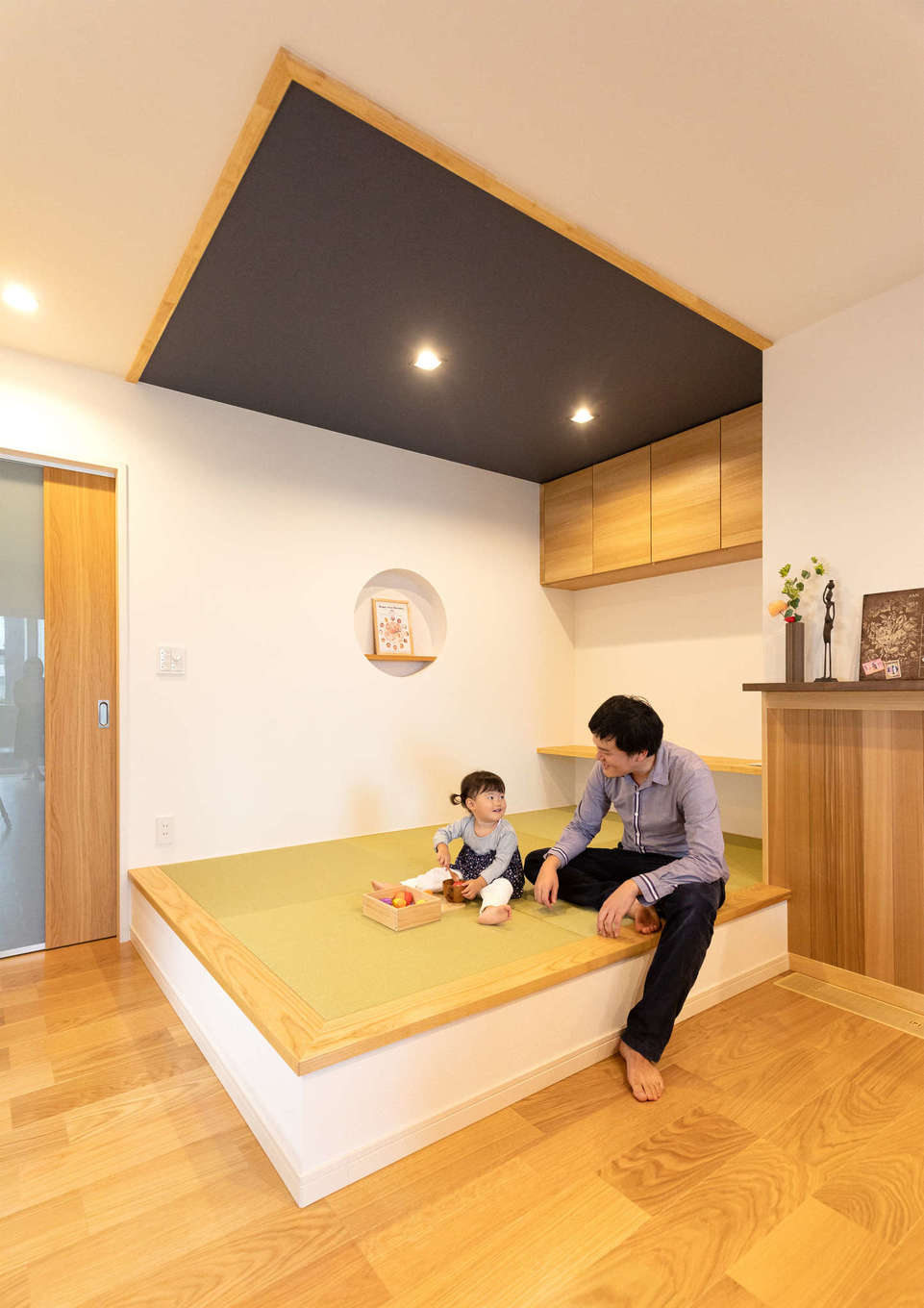 Yamaguchi Design 【省エネ、間取り、平屋】リビングの一角にしつらえた小上がりの畳コーナー。子どもと遊んだり、ご主人がゴロンと横になったり、ゲストが椅子代わりに使ったりと大活躍。まあるく切ったニッチと天井のクロスがアクセントに