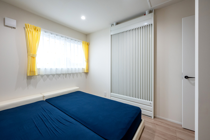 明るい寝室。黄色のカーテンがアクセントとなり、シンプルながらも温かみのある空間が広がる。充分な収納スペースも確保されている。