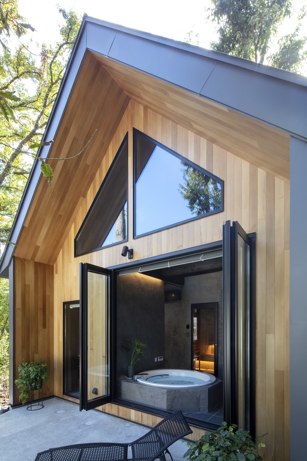 木製の外壁に調和した大きなガラス窓が特徴の浴室。開放的な空間が広がり、周囲の自然を楽しみながらリラックスできるデザイン。