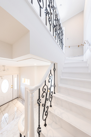 白と黒のコントラストが美しい階段スペース。吹き抜けのデザインとアイアンの手すりが調和し、上品な雰囲気を演出する。