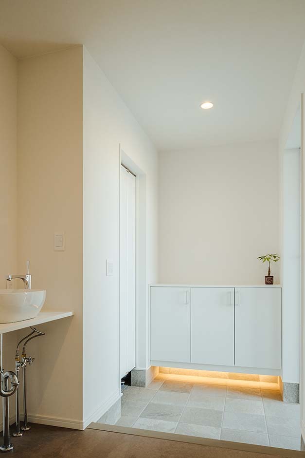 間接照明がオシャレな雰囲気をつくる玄関ホール。子どもや来客のために洗面を設置し、白で統一することですっきりした印象に