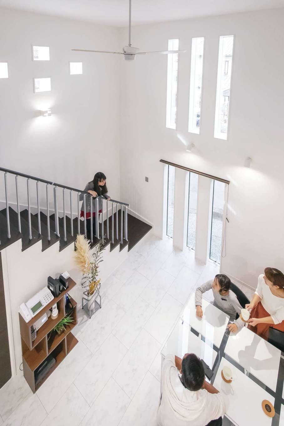 アフターホーム【デザイン住宅、二世帯住宅、間取り】リゾートホテルのような心地よさをもたらす吹抜けのダイニング。三連のスリット窓でプライバシーを守りながら開放的に過ごせる。デザイン階段がアクセントに