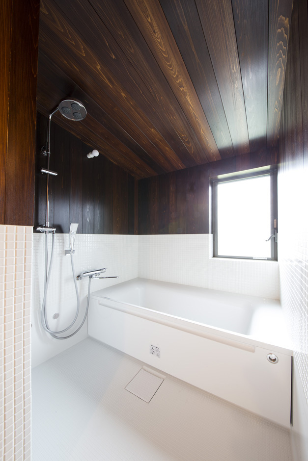勾配天井のハーフユニットバス。天井と壁は風呂桶に使われるサワラを漆塗りしたもの。雨に打たれる感覚のシャワーヘッドもマッチしている。和と洋が絶妙に融合した浴室は、極上のバスタイムを楽しめそう