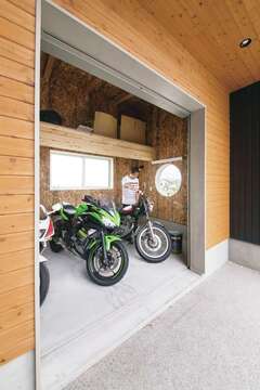 ７畳のバイクガレージは、３台分のバイクをゆうに格納できる広さ。道路側に丸窓を設けたのはご主人のこだわり。荷物をしまえる棚も設けてある