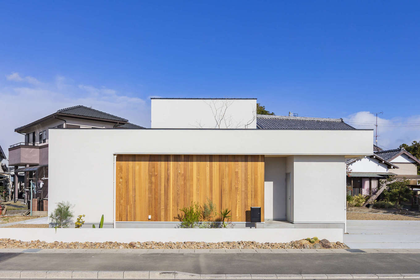 ARRCH アーチ【デザイン住宅、間取り、平屋】白い箱型のフォルムに、板張りの壁が映えるスタイリッシュな外観。浜松環状線に面した部分には開口部を設けず、プライバシーに配慮。板張りの壁の奥が玄関。玄関の横には外収納が設けてある