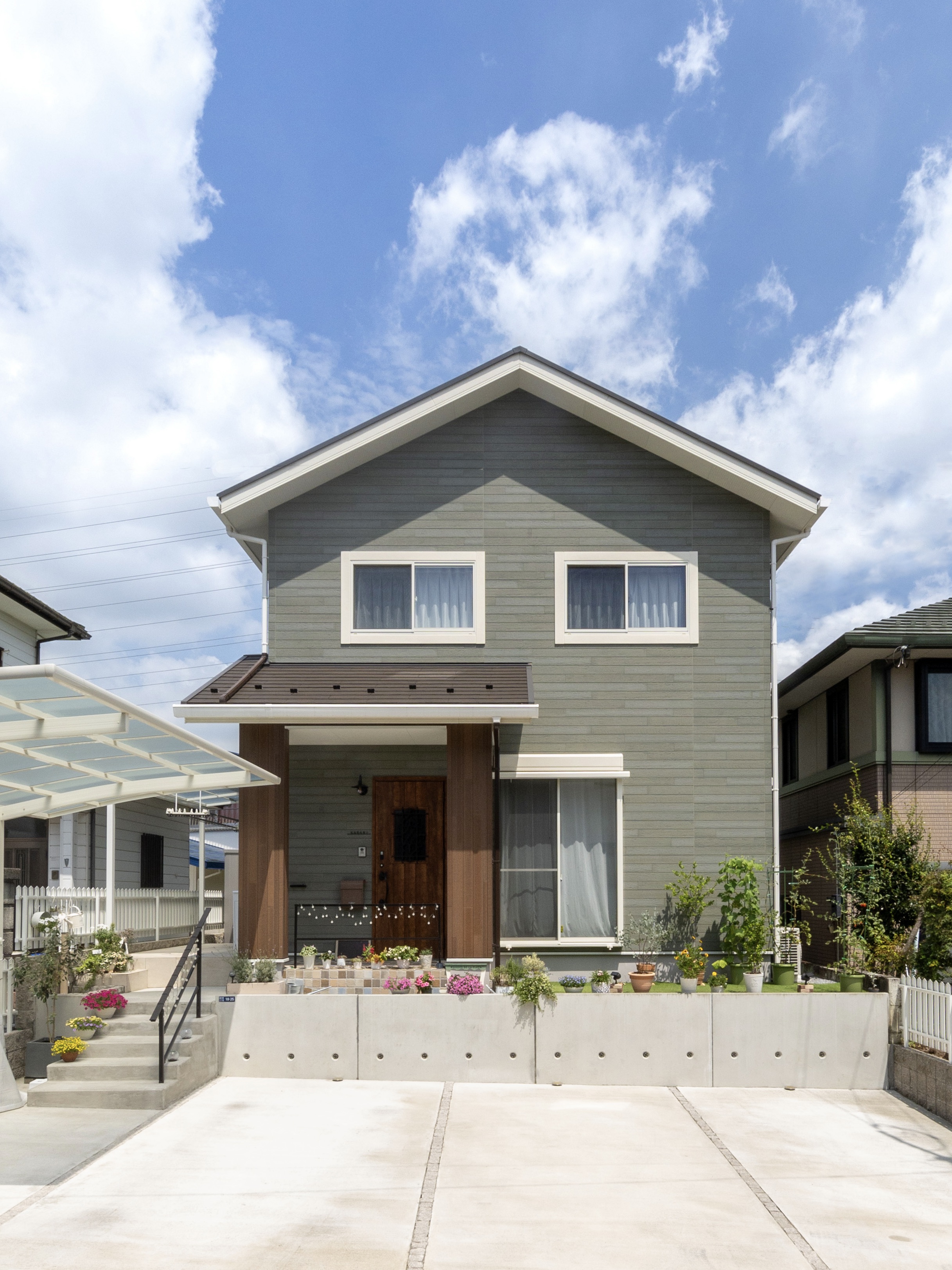 エスホーム｜シンプルでモダンなデザインの二階建て住宅。整然とした外観が魅力であり、庭の植栽が彩りを添えている。空に映える色合いが美しい。