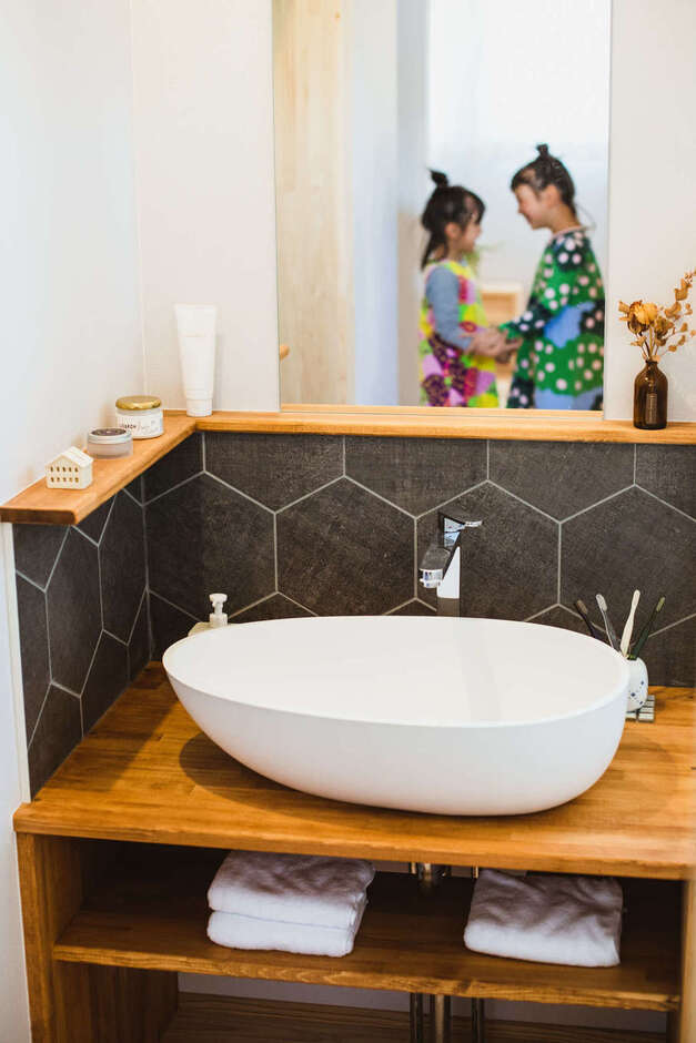 デザインと使い勝手を両立した造作の洗面台。水はね防止のタイル、かわいいフォルムのボウル、鏡の形状、収納など、ディテールにまでとことんこだわり、熟練大工の技でていねいに仕上げた