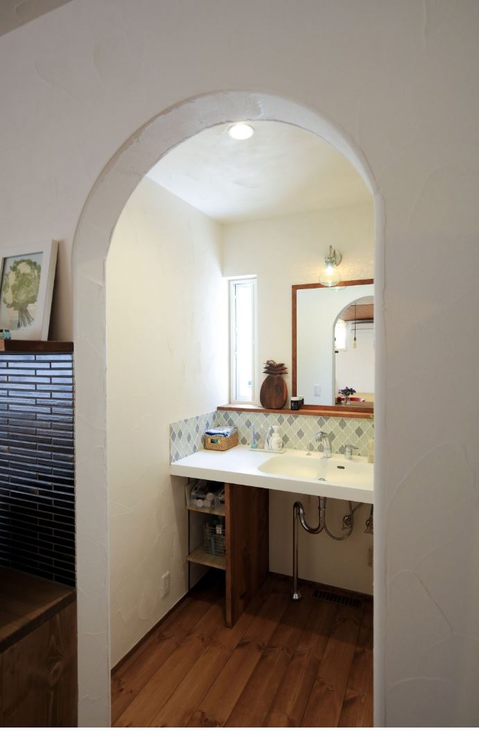 アイジースタイルハウス【自然素材、間取り、平屋】アーチの垂れ壁で緩やかに仕切られた洗面室。カウンターは車椅子でも楽に使えるよう、高さと奥行きに配慮した。やさしい色合いのタイルがアクセントに。脱衣室と離したことで、誰かが入浴中でも手洗いや歯磨きが可能に