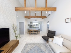 開放的なリビングダイニング。木の梁がアクセントになり、自然光がたっぷり注ぐ空間。ダイニングテーブルとソファがバランスよく配置されている。