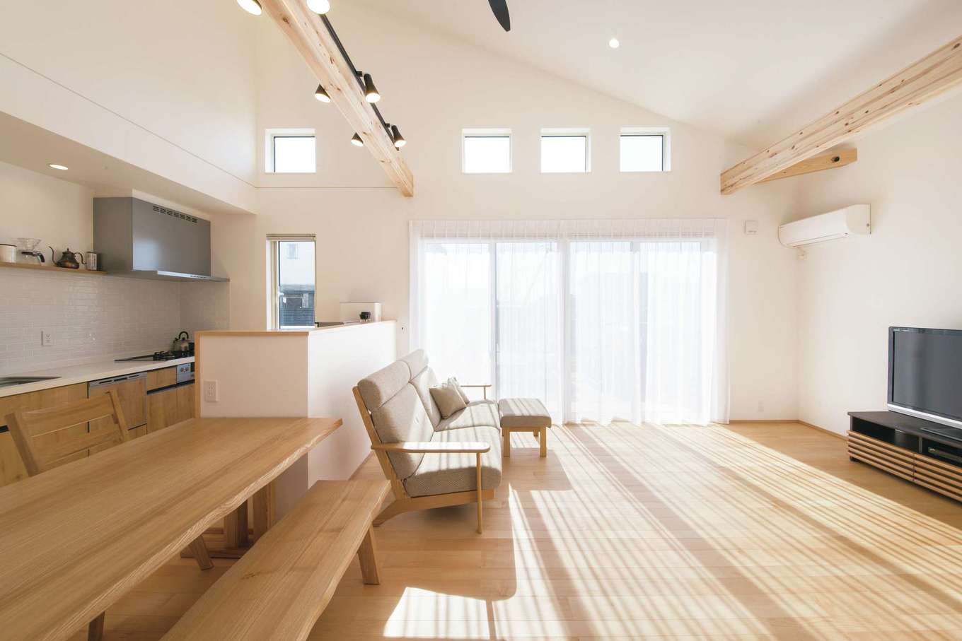 コットンハウス【子育て、省エネ、間取り】屋根勾配を活用した伸びやかで明るいLDK。高窓は視線を気にせず採光できるのが利点。照明を設置するために飾り梁を渡し、キッチン壁はタイルで上品に仕上げた