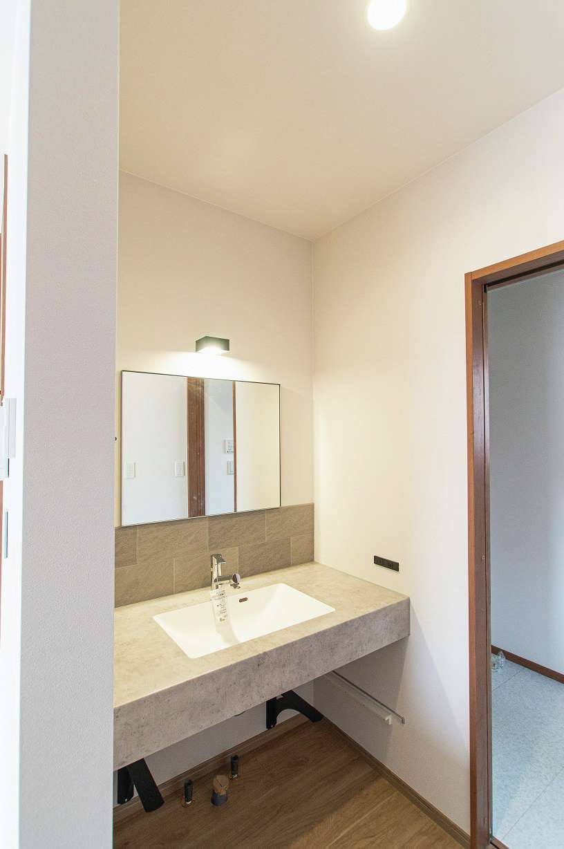 さくらホーム【デザイン住宅、収納力、間取り】モデルハウスで見た、キッチンと脱衣所の動線上の配置を参考に造作した洗面台。鏡は施主支給で対応した。ワイドサイズで使い勝手が良く、壁の立ち上がりのタイルは、水跳ね防止とデザイン性を両立