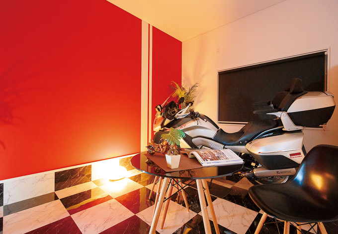 ご主人の夢を叶えたビルトインのバイクガレージは、1600ccのBMWが余裕で収まる7.2畳。ブラック＆ホワイトのフロアタイルが高級感を演出。鮮やかな赤い壁と白のラインの組み合わせは前嶋社長のセンス。バイクがない時は、おうちカフェとしても使えそう