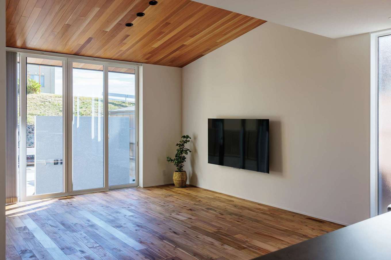 tact design firm【デザイン住宅、間取り、インテリア】ダイニングと天井高を変えたリビング。勾配天井に張ったマホガニーを軒天にも使うことで視線が伸びていき、より開放感が生まれた。外構に塗り壁の塀を設け、外からの視線をカットしつつおおらかに暮らすことができる