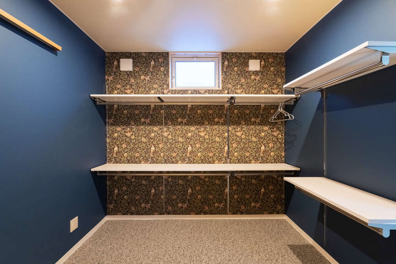 ALAIN（アラン）｜２階の洗面コーナーに隣接したファミリークローゼットには、家族3人分の衣類をまとめて収納。英国ウィリアム・モリスの深みのあるブルーのクロスと壁紙、グレーの床と白い棚を組み合わせ、独特の世界観を演出。プライベートな空間に遊び心を詰め込んだ