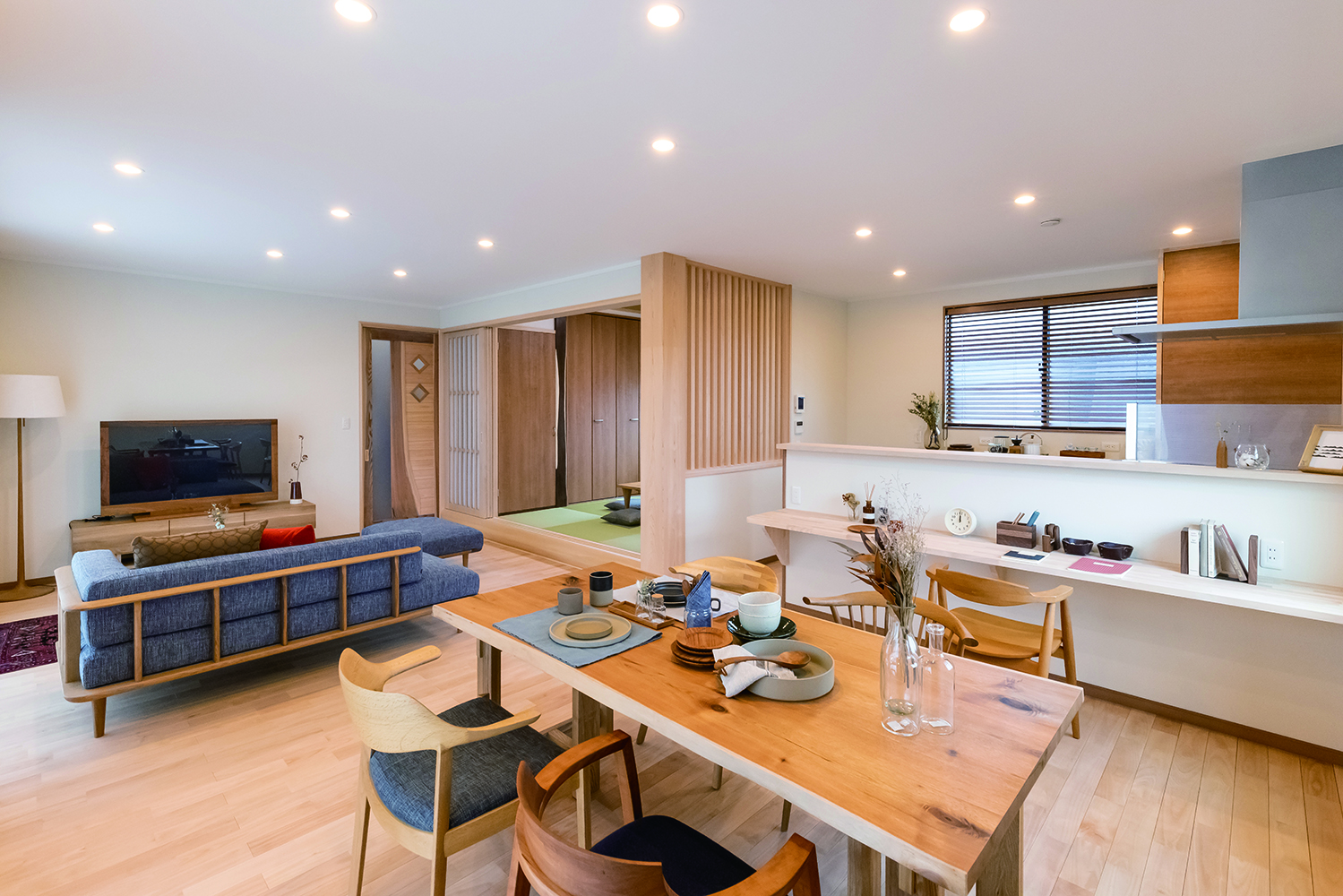 住まいるコーポレーション【自然素材、省エネ、夫婦で暮らす】LDKの床は樺桜（カバザクラ）の天然木を使用。広さにゆとりを持たせ、リビングやダイニングでゆったりとくつろげるようにした。小上がりの和室や格子の壁など和のテイストも取り入れて、上品で落ち着きのある空間を演出。壁には珪藻土を用い、雨天時もジメジメ感なく快適