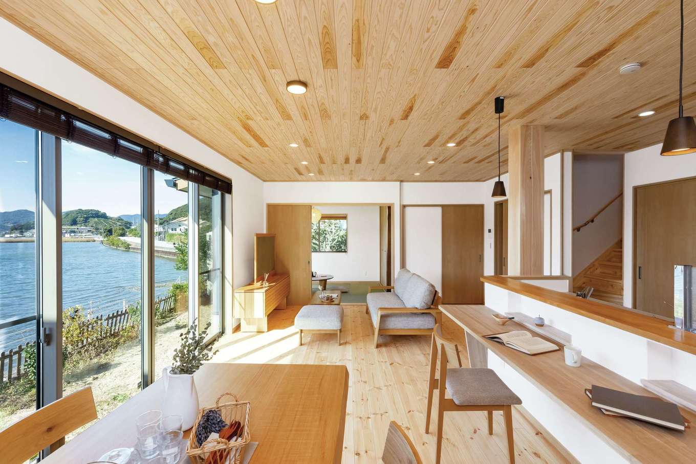 住まいるコーポレーション【収納力、自然素材、間取り】松の床と杉の天井、珪藻土の壁を用い、自然素材のすこやかさに癒されるLDK。目の前に広がる浜名湖の風景を眺めて、リゾートチックな日常を楽しめる。ダイニングから和室の窓に至る抜け感も爽快だ