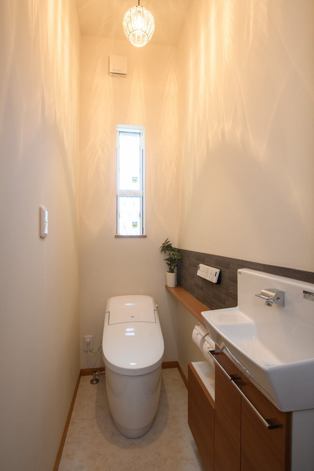 Sus∞Eco Home（サスエコホーム）｜コンパクトながらも明るいトイレ空間。木目調の収納と洗練された手洗いスペースが機能的でスタイリッシュな印象を与える。