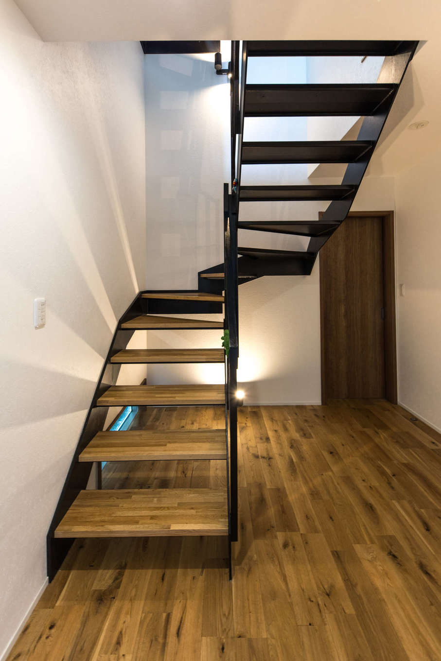 建築システム（狭小住宅専門店）【狭小住宅、間取り、屋上バルコニー】空間を広く見せる開放的なスケルトン階段。アイアンと木調で、LDKと同じヴィンテージ調に統一した。階段下の地窓と照明で足元から明るさを届ける