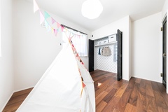 明るい光が差し込む子ども部屋。柔らかい色調の床と白いテントが遊び心を引き立てており、収納スペースも整理整頓しやすいデザインである。