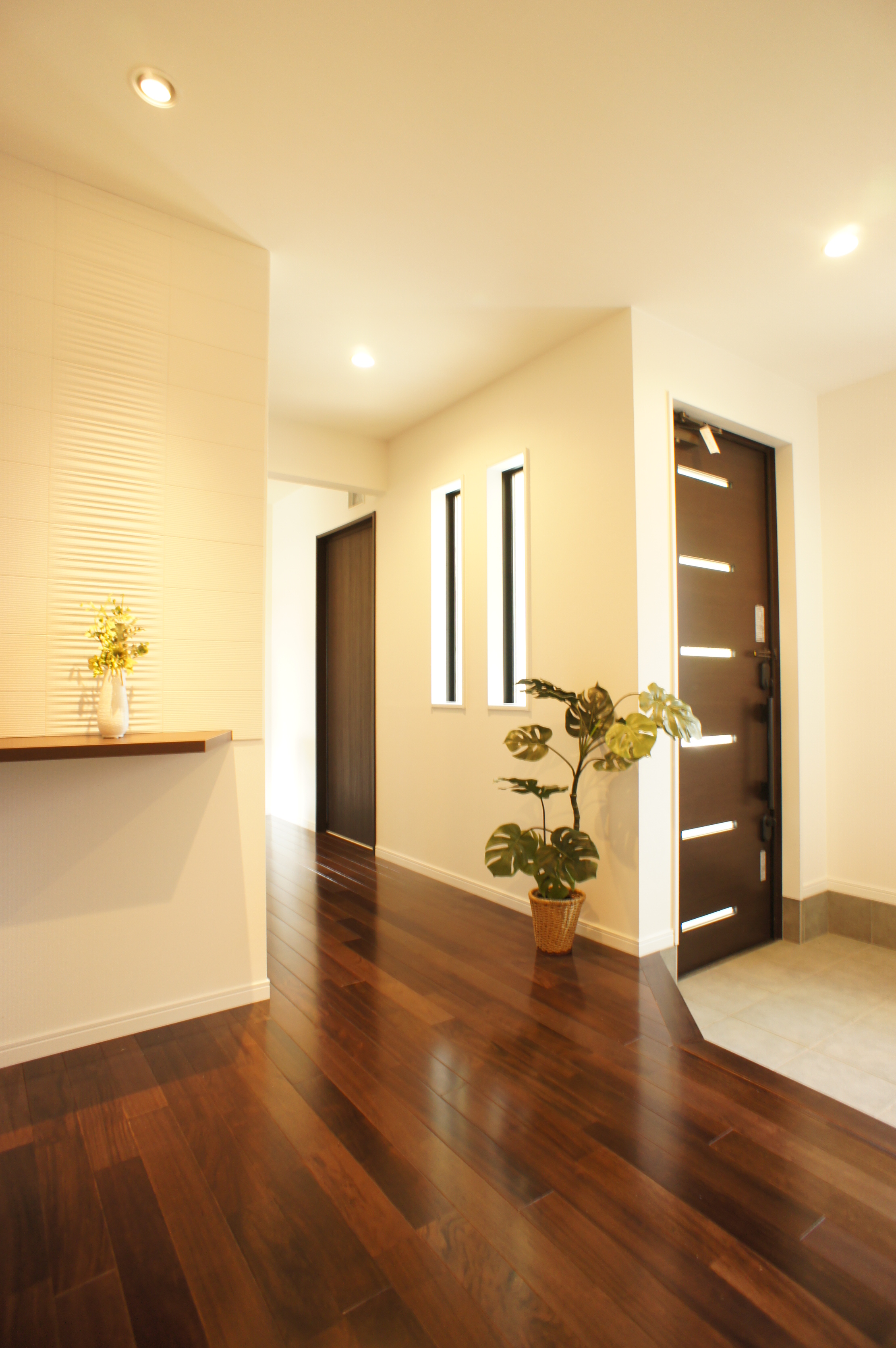 小野田産業～designers house project～｜明るく開放的な玄関ホール。シックなフローリングとナチュラルな観葉植物が、訪れる人を暖かく迎える空間を演出している。